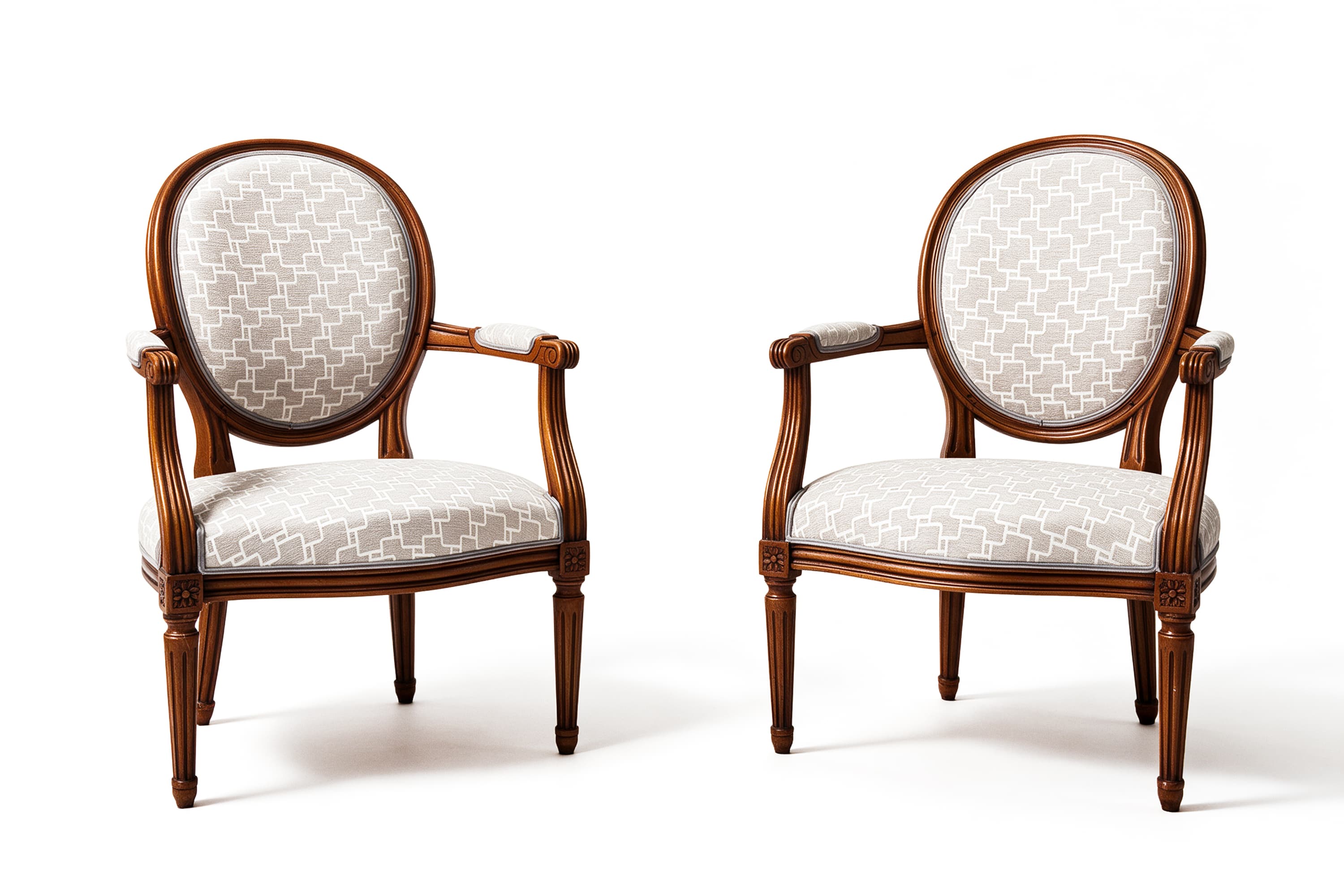 Deux fauteuils médaillon en bois teinté, garnis d'un tissu gris clair à motif géométrique blanc, sur fond blanc.